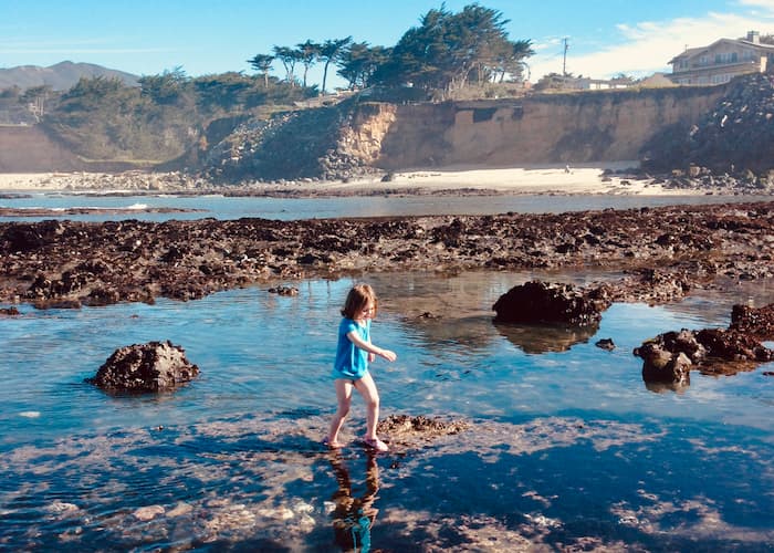 girl walking in tidepools with bluffs in background
