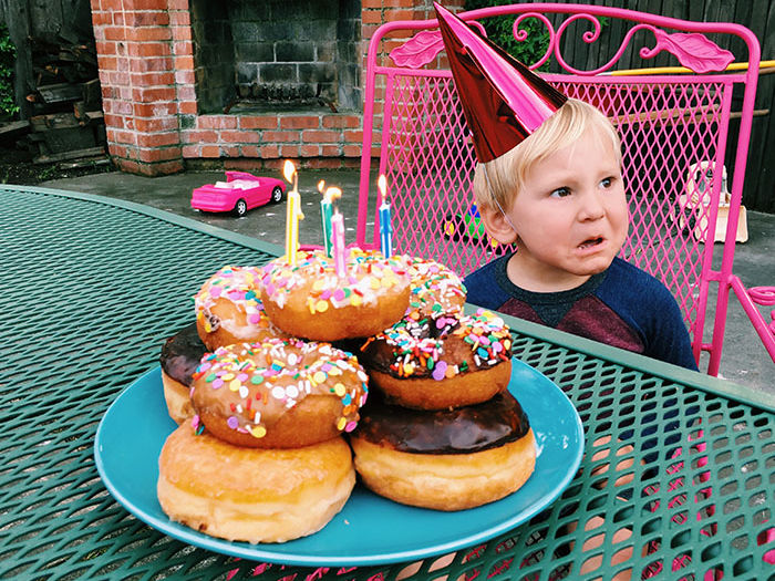 child in party hat with crabby face and plate of donuts