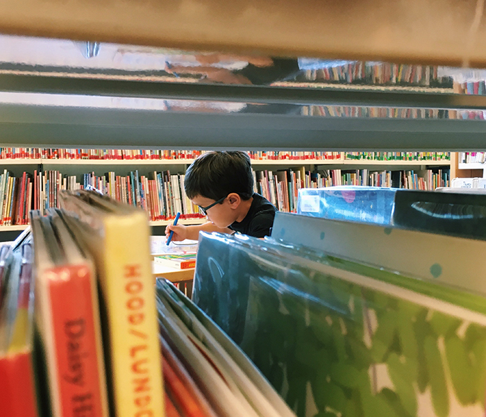 child at library with stacks of books