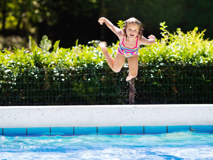 Happy little girl jumping into outdoor swimming pool in a tropical resort during family summer vacation. Kids learning to swim. Water fun for children.