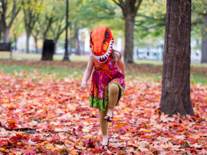 child in dinosaur costume stomping in leaves