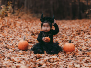 baby in devil costume sitting among leaves