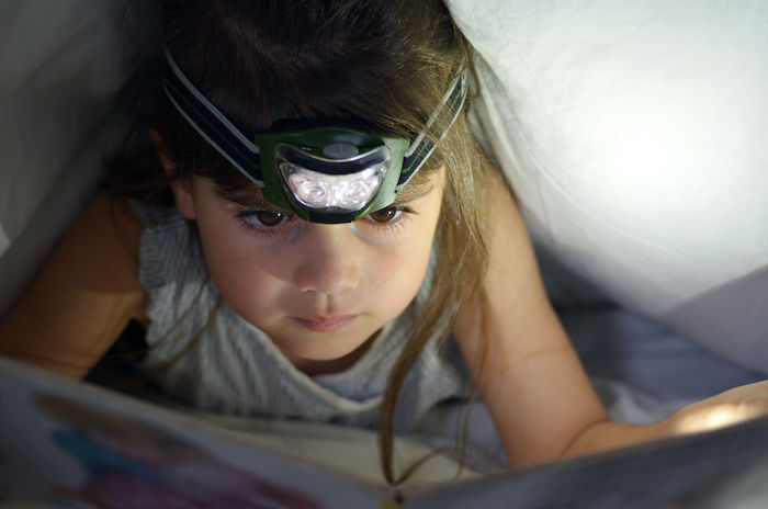 child reading by headlamp - library games