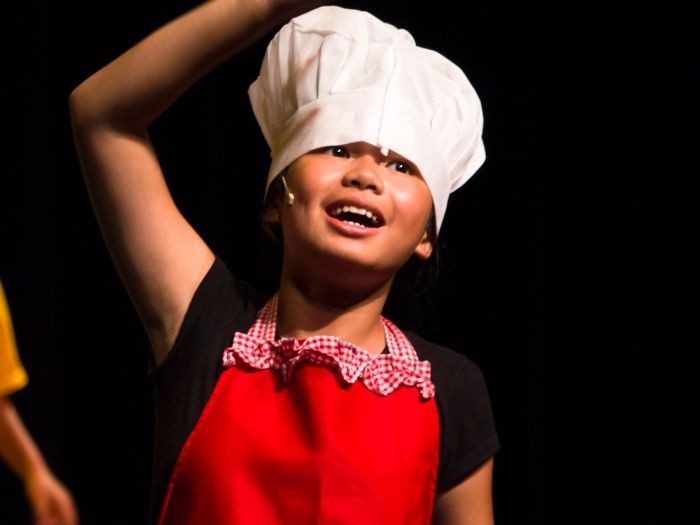 31 Things to Do With Bay Area Kids in March 4 A 9 year old child with a white chefs hat and a red apron has their hand up and is singing.