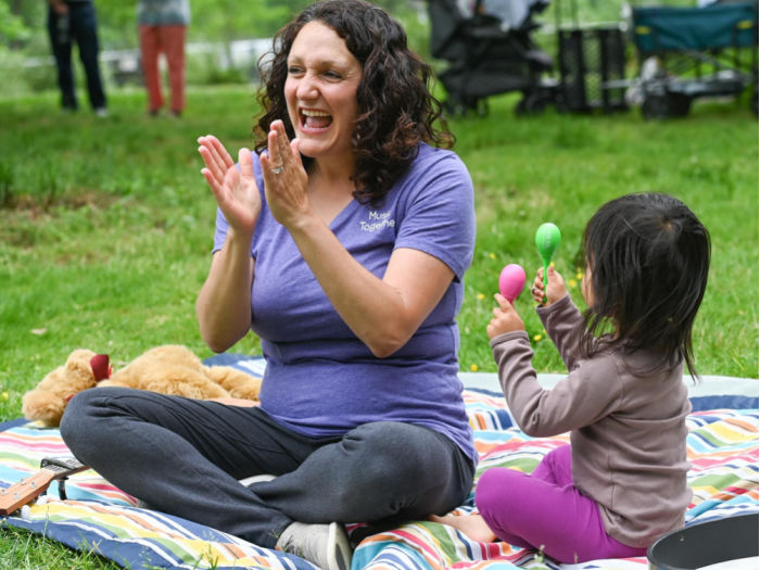 teacher and child making music outside on blanket