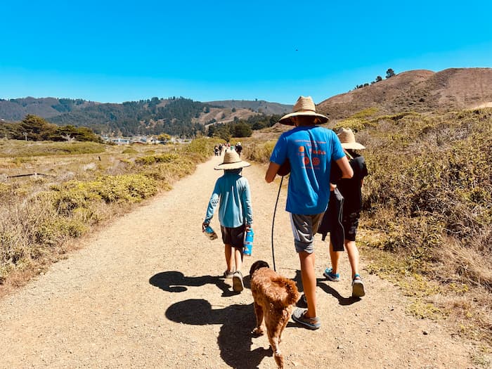 three kids in hats walking a dog on a trail