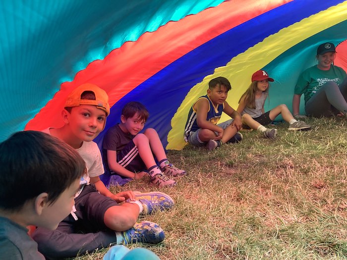 camper children and CIT named Grace are under a giant colorful parachute