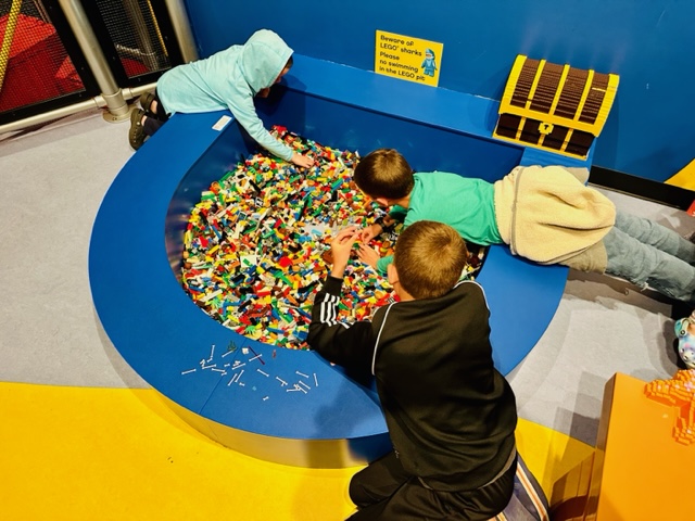 three kids leaning over LEGO pit