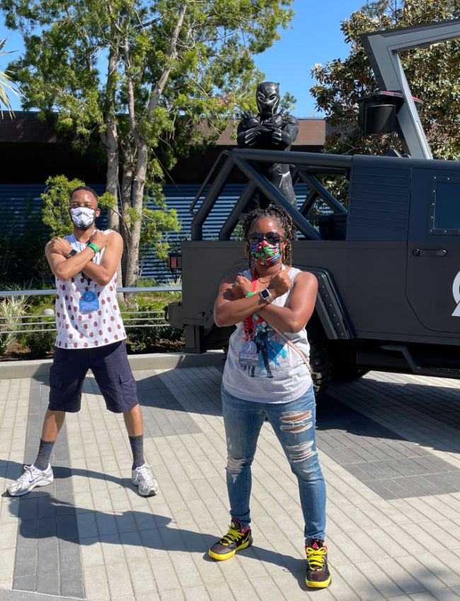 two people crossing arms in wakanda salute in front of T'Challa statue