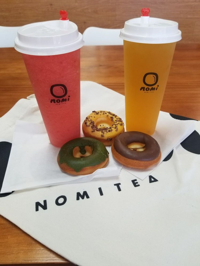 Two Nomi Tea boba drinks with three mochi donuts on a table