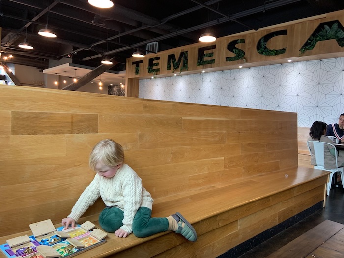 child on long bench doing a puzzle he doesn't know he's at a cafe