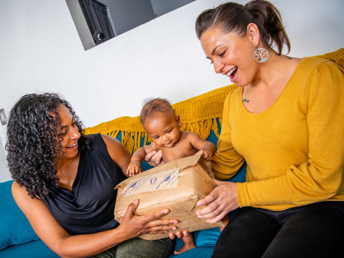 two moms and baby with pack of diapers