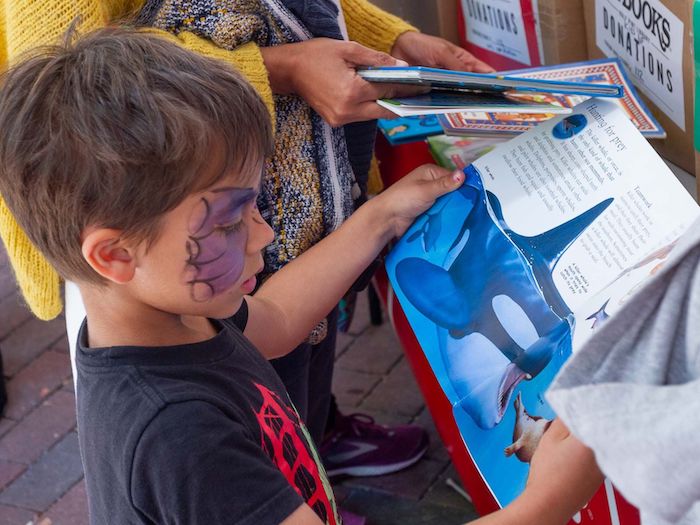 child with face paint reads outdoors