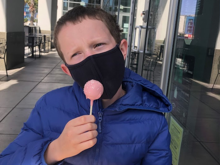 child in mask eating cake pop