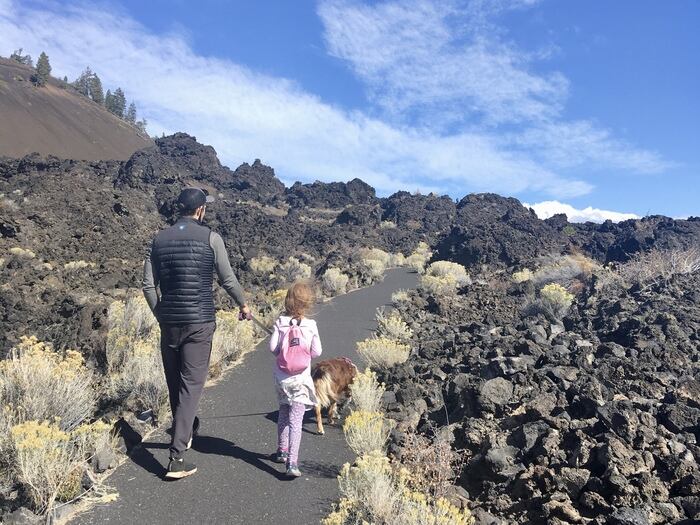 Child and adult walk dog through lava rock field