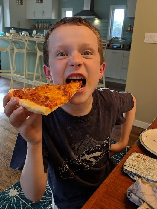 Kid taking a bite of pizza slice at home