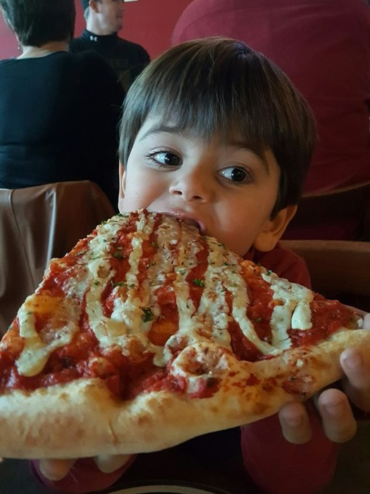 Kid biting into a slice of Bobby G's pizza