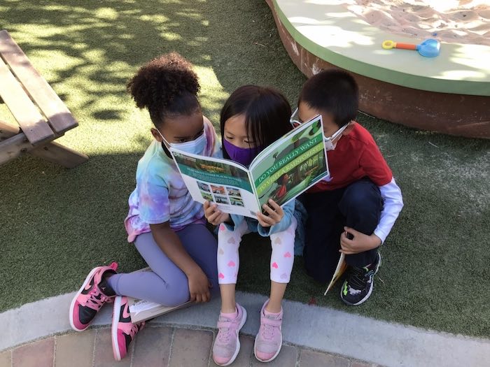 three children reading together outside