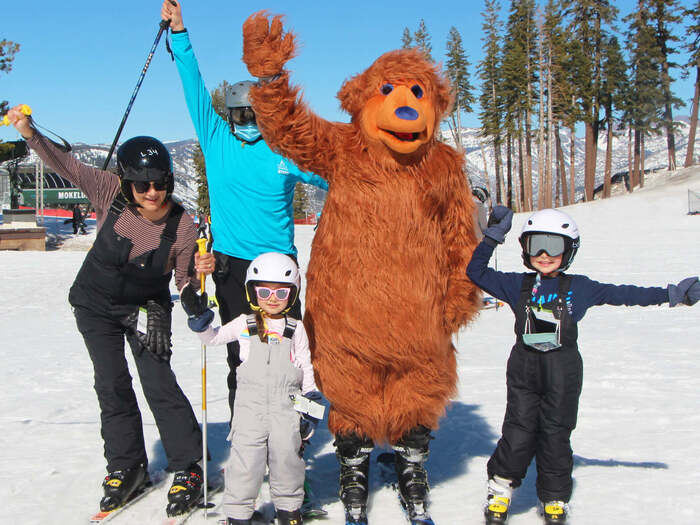 Family on skis poses next to Person dressed in bear costume