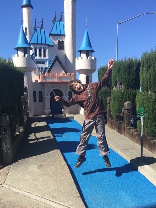 Child jumps for joy while mini golfing with castle in background