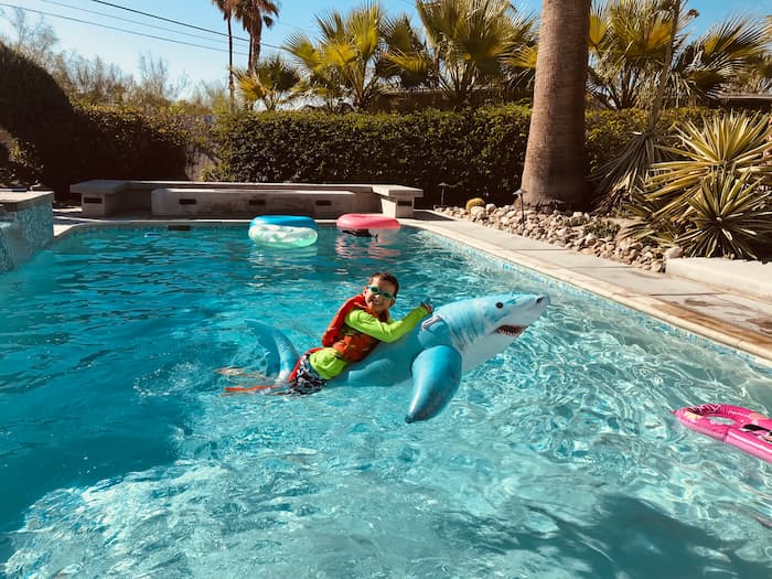boy riding inflatable shark in pool