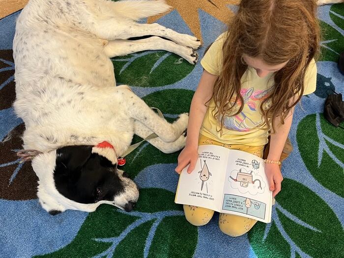 Child reading a book to a dog