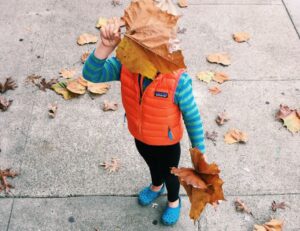 city kid playing in the autumn leaves