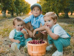 three young boys eating cherries from a basket