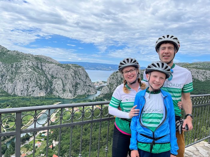 two adults and one child wearing bike clothes stand in front of an overlook