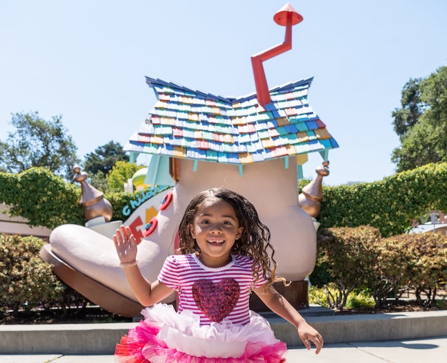 child running toward camera with fairyland iconic shoe in background. she is wearing a heart on her shirt