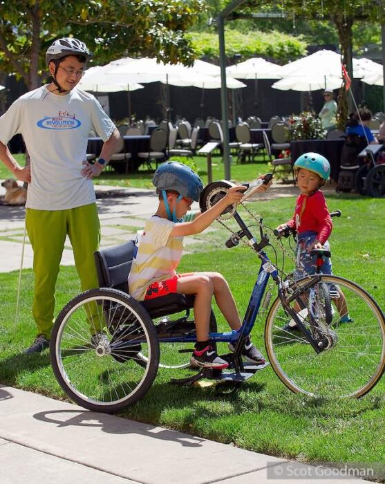 adaptive cycling, two children and an adult, green grass