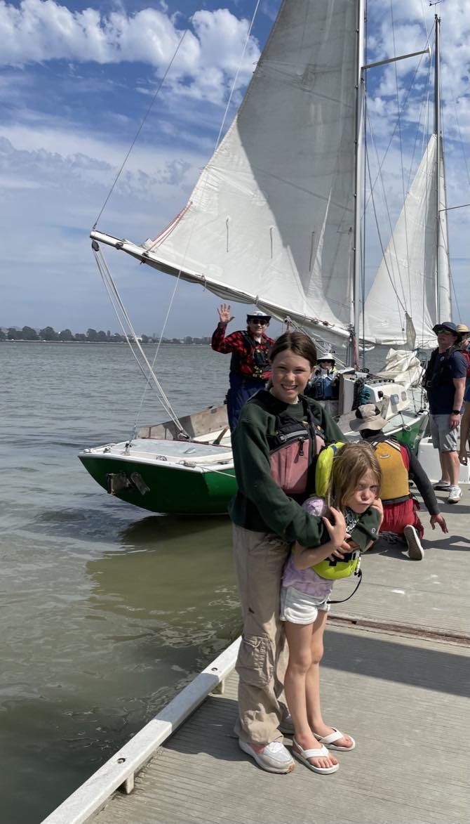 two kids hugging, sailboat and water behind them