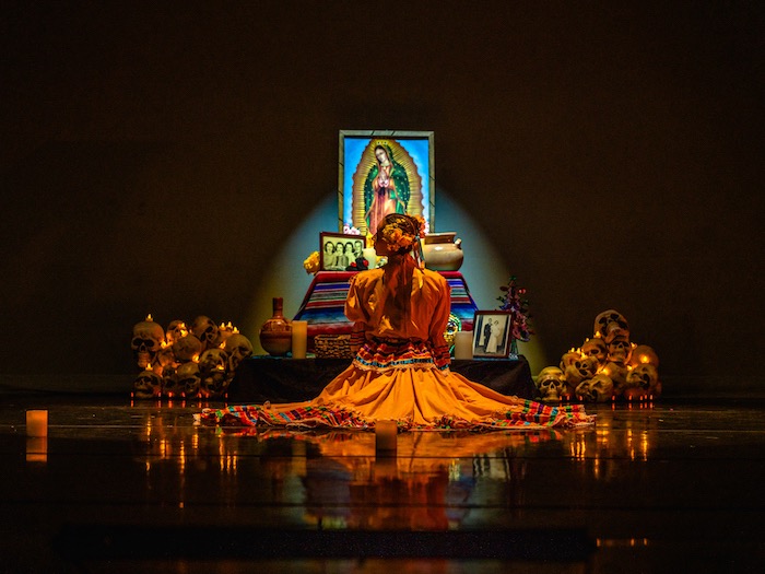 dia de los muertos dancer in front of a glowing ofrenda with skulls