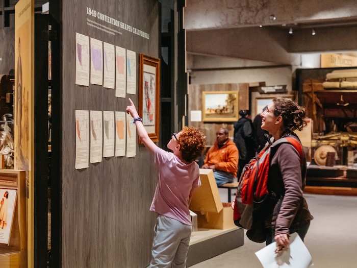 Parent and child interact with California History exhibit at Oakland Museum of California
