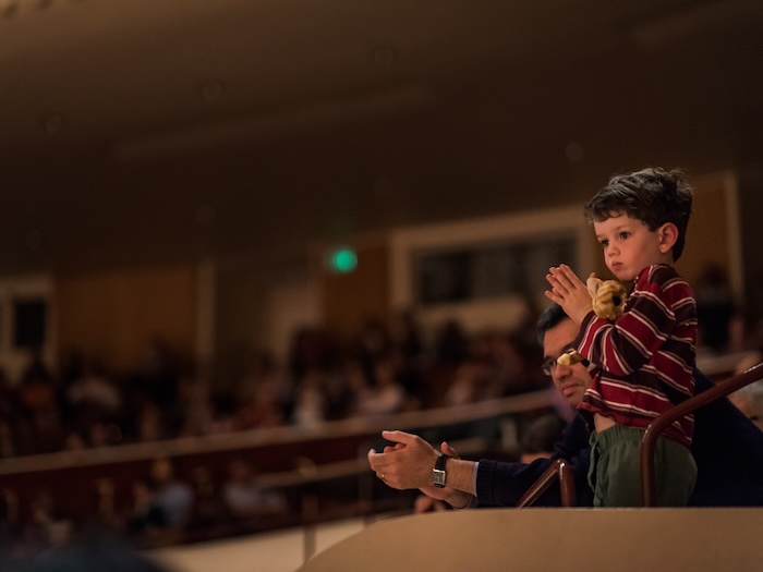 child watches the sf symphony from the balcony with a stuffed animal
