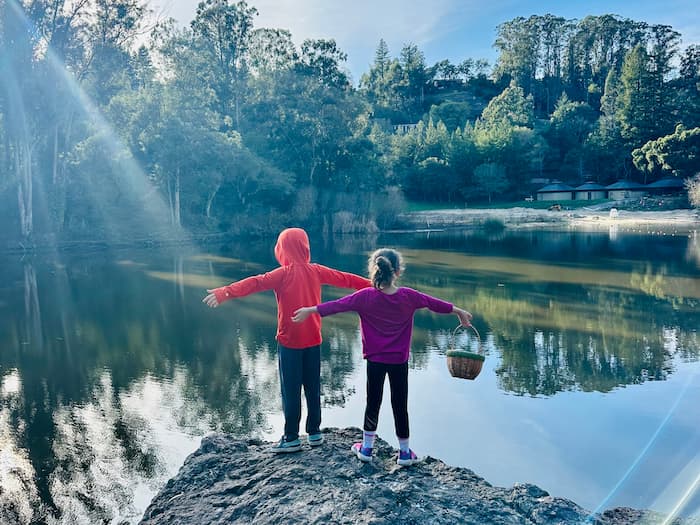 two kids with their arms spread out in front of a lake