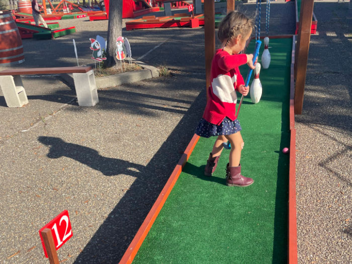 three year old playing mini golf with bowling pins as obstacles at putters goat track in alameda
