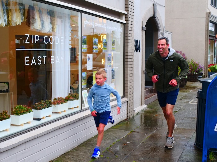 parent and child running past the zip code east bay storefront window