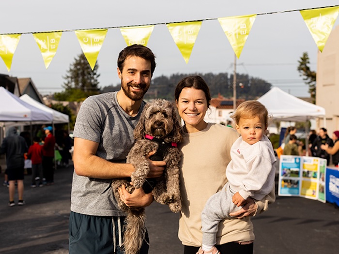 two parents, one kid, one dog standing outside together