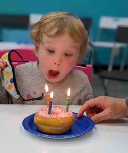 child blowing birthday candle on a donut