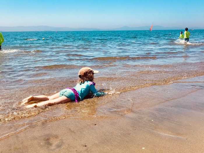 little girl laying the shallow water at the beach