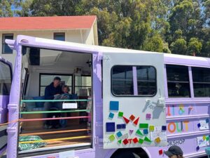 lavender painted school bus decorated with words OUT AND ABOUT filled with books. parent and child reading together