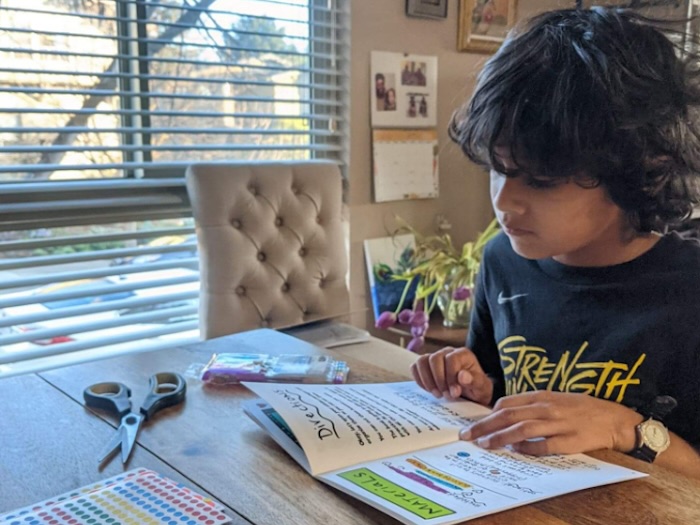 art student working on art explorations at home with workbook, scissors, and stickers