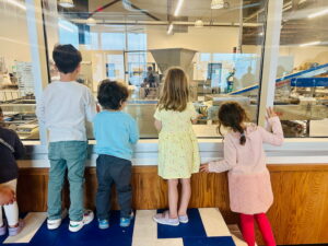 kids standing at window watching bagel factory machine