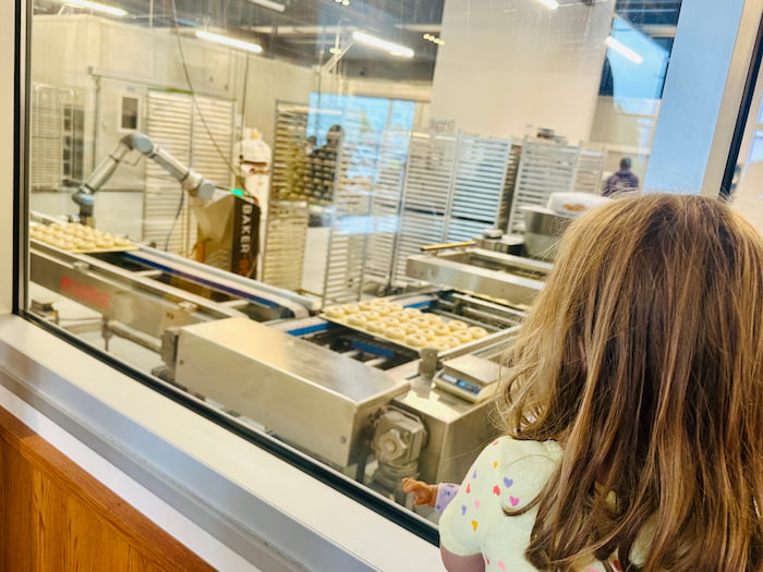 little girl watching bagel machine through window