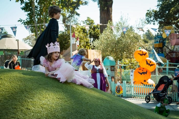 child in princess halloween costume plays on the ground at fairyland