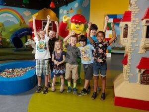 kids are happy in casual clothes in front of a costumed lego character in a lego play space