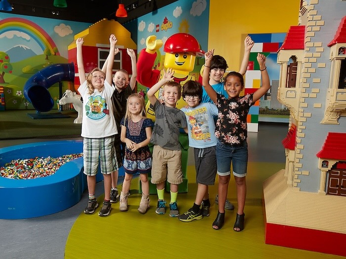 kids are happy in casual clothes in front of a costumed lego character in a lego play space