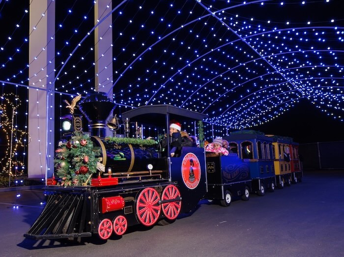 illuminated christmas train with no track driving under a light tunnel