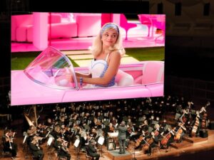 barbie movie on screen above symphony orchestra